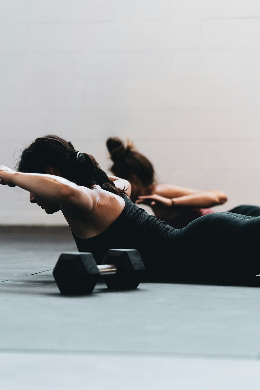 Two women planking on the floor, dumbbells beside them